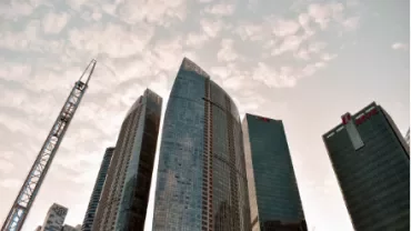 Skyscrapers with a crane in the foreground under a cloudy sky.
