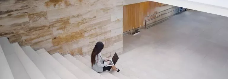 A woman using her laptop while sitting on a staircase, appearing engaged in her work.