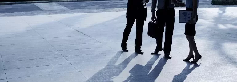Three business professionals standing together in front of a modern office building, engaged in conversation.