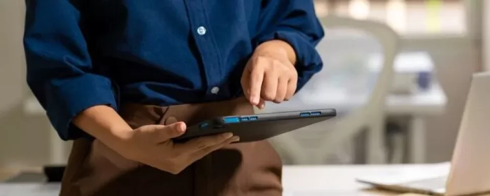 Individual displays a tablet in front of a laptop, illustrating the use of multiple technology tools.
