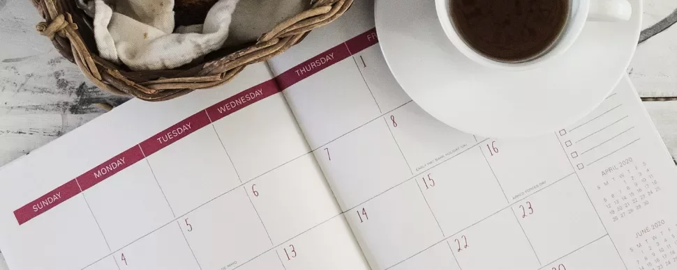 Open calendar with a coffee and bread basket on a table.