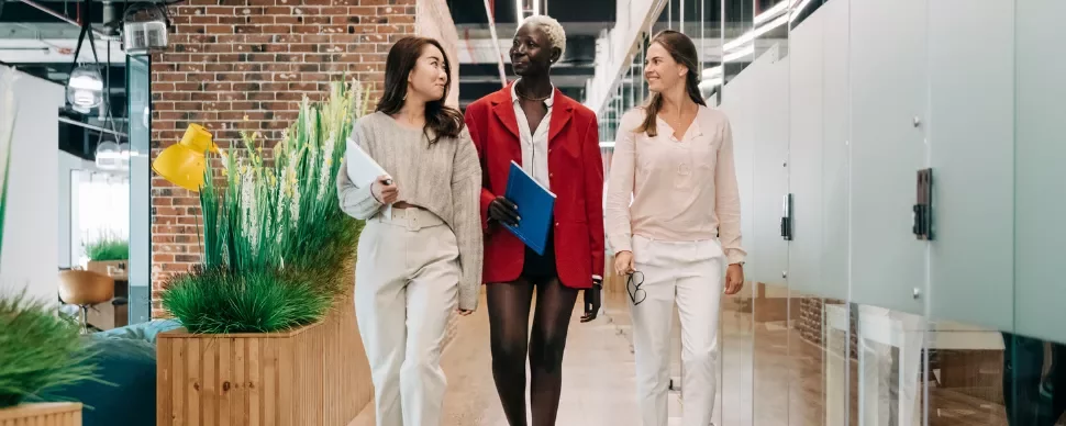 Three colleagues walking and talking in a modern office corridor.