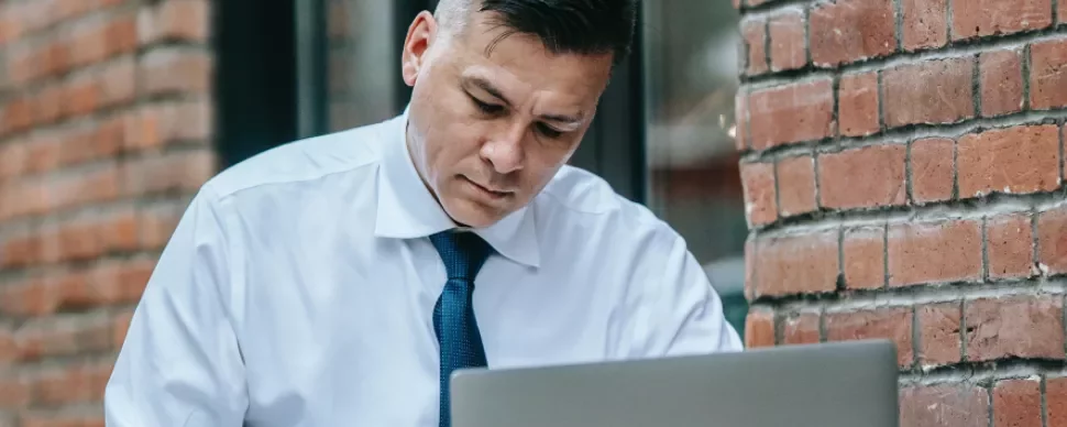 Man in white shirt and tie working on a laptop outdoors.