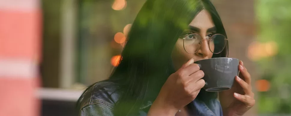 Person with glasses enjoying a hot drink in a serene setting.