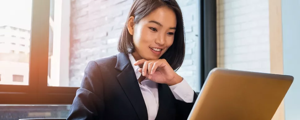Professional woman in a suit smiling at her laptop in an office.