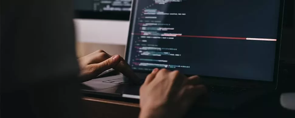 Person typing code on a laptop in a dimly lit room