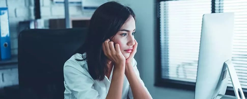 Woman in a white shirt looking thoughtfully at a computer screen in an office.