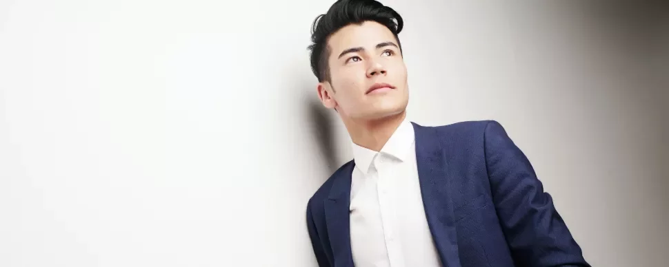 Man in a blue suit looking upwards against a white background.