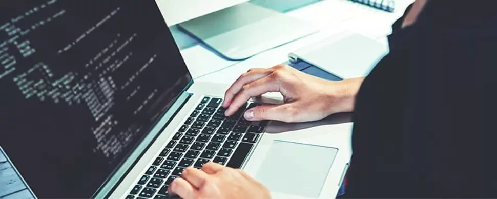 Person typing code on a laptop at a desk.