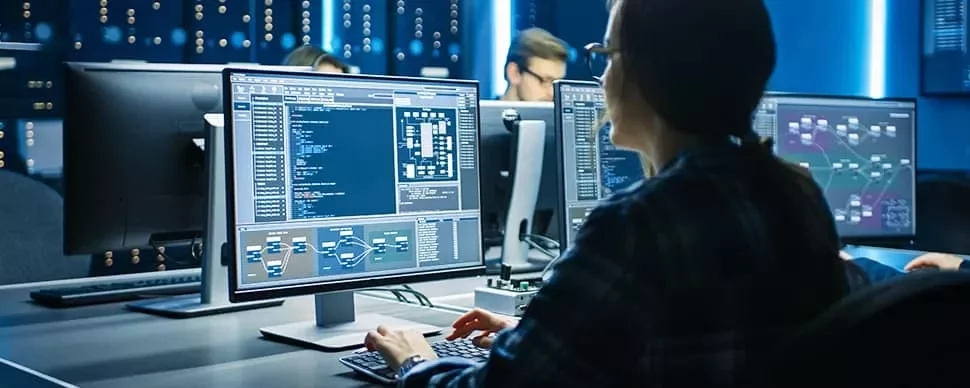 Person working at a computer with multiple screens displaying code and data diagrams.