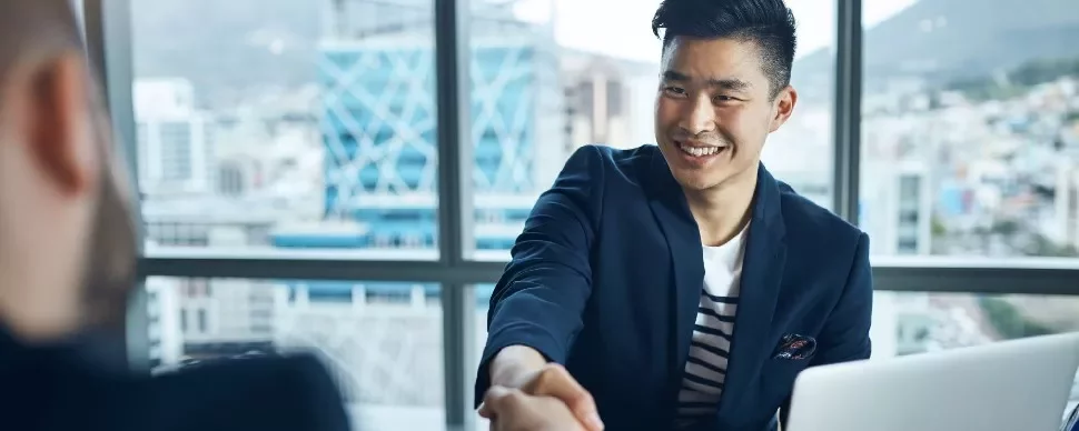 Smiling man in a suit shakes hands at a meeting in modern office.