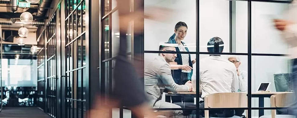 Team meeting in a glass-walled office with four people discussing.