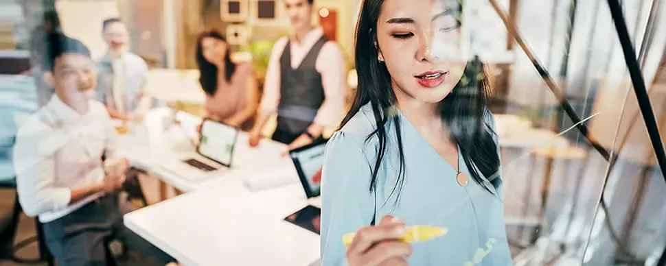Woman writing on glass board during meeting.