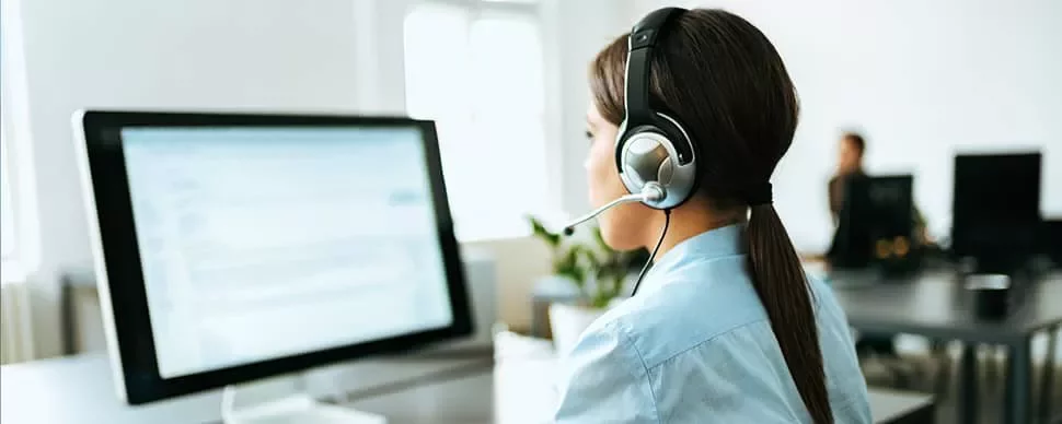 Woman wearing headset working at a computer in an office.