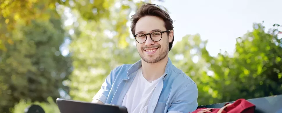 Man with glasses smiling while using a tablet outdoors