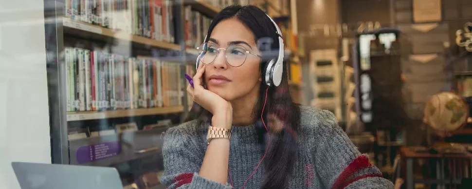 Woman in a library wearing headphones, gazing thoughtfully.
