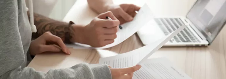 Two people working with documents at a desk near a laptop.