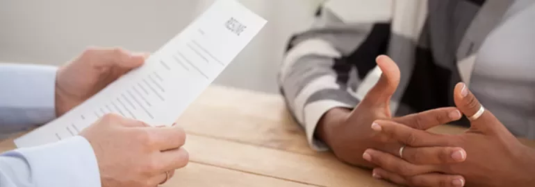 Close-up of a job interview with resume and gesturing hands at a table.