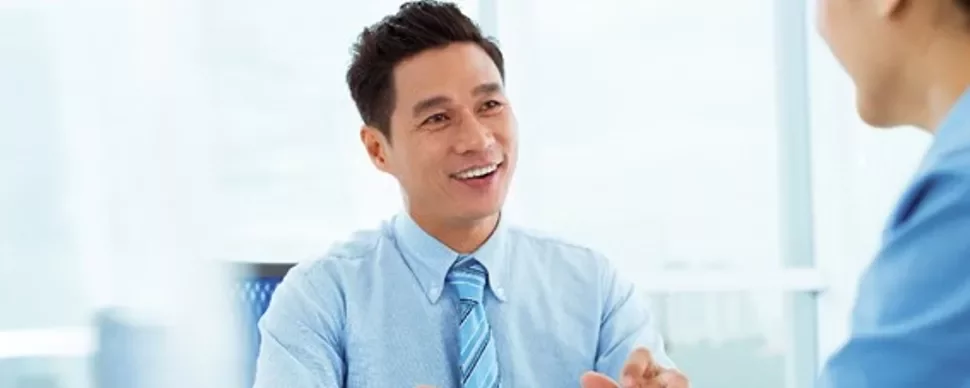 Smiling man in a business meeting, wearing a blue shirt and tie.
