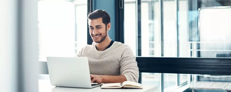 Man smiling at a laptop in a bright office.