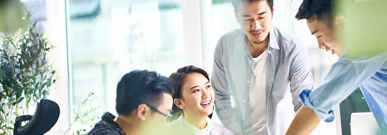 A group of four people collaborating in a bright office with plants.