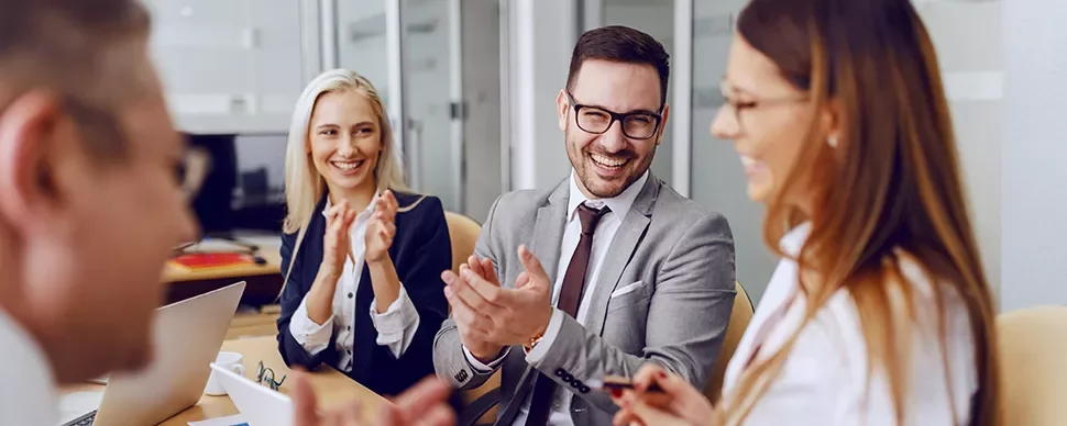 Business meeting with four people clapping and smiling.