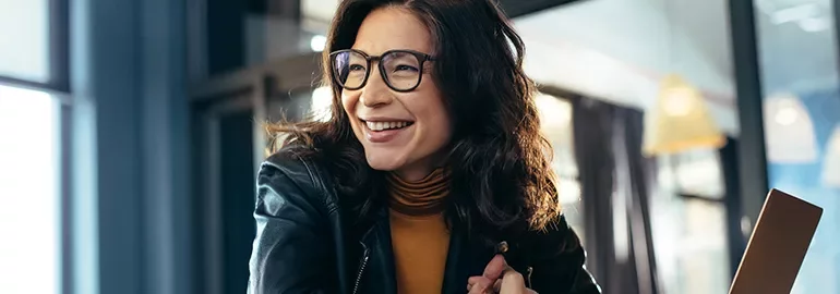 Woman in glasses smiling indoors with warm lighting.