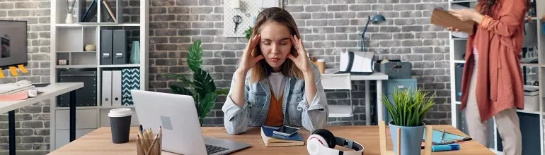 Woman at desk looking stressed with laptop and headphones.