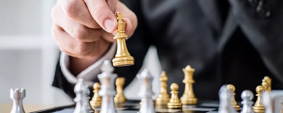 An image of a hand playing a gold-colored chess pawn.