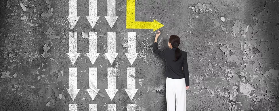 An image of a person standing facing a wall pointing at a yellow arrow to the left against white arrows pointing downwards