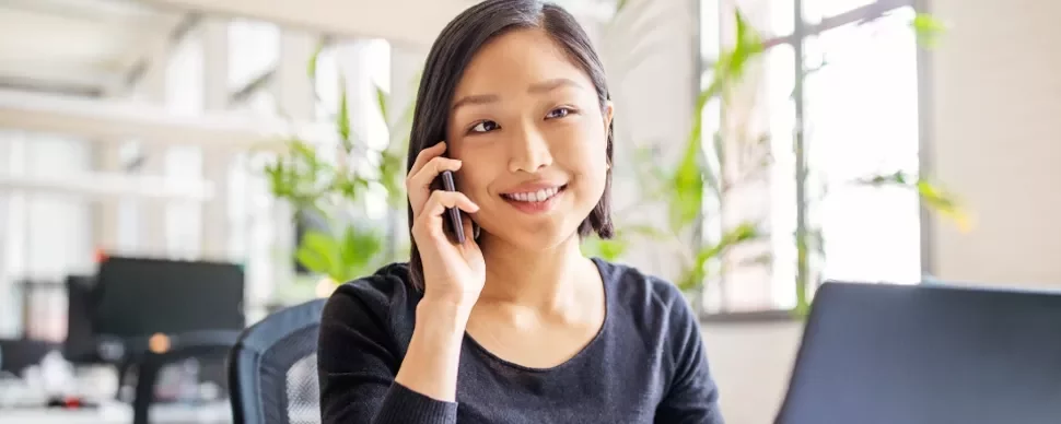 female Chinese white-collar professional in her 30s answering her mobile phone while sitting in front of the laptop