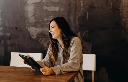 A female Personal Assistant smiling cheerfully while holding a smart tablet.