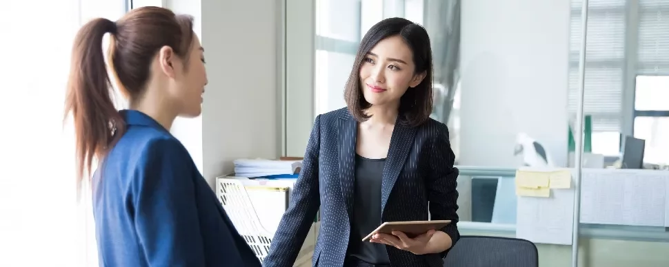 Two professional ladies having a conversation in an office room about succeeding as an office manager.
