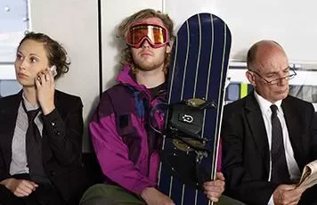 Three people sitting on a bench; a woman on the phone, a man in ski gear, and a man reading a newspaper.