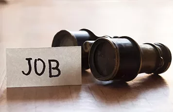 Close-up of binoculars next to a card reading 'JOB'.