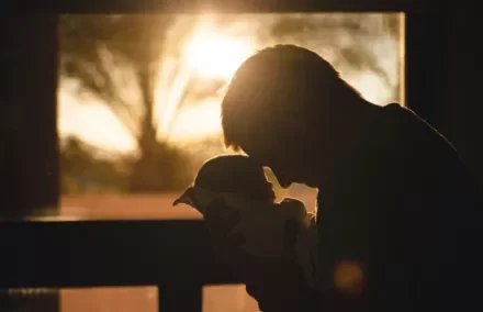 Silhouette of a parent holding a baby against sunset light.